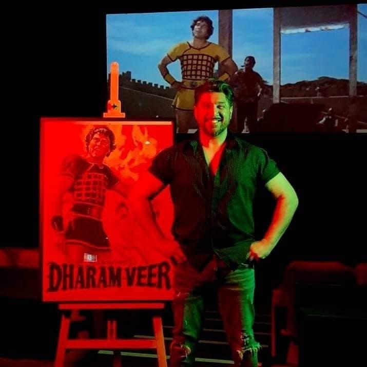 Mak Singh today, beside a Dharam Veer poster